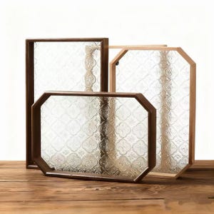 Può includere: Tre pannelli decorativi in vetro con cornice in legno. Le cornici hanno varie forme, tra cui rettangolare e ottagonale. Il vetro presenta un motivo floreale. Le cornici sono in tonalità marroni e legno naturale. I pannelli sono esposti su una superficie di legno.