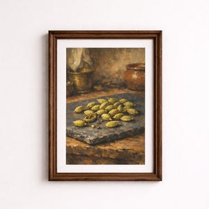 Op de afbeelding: Een ingelijst olieverfschilderij met een stilleven van een groep groene kardemompeulen op een donkergrijze stenen plaat. Op de achtergrond staan een metalen vijzel en een kleine bruine keramische pot op een houten ondergrond.