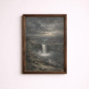 Op de afbeelding: Een ingelijst landschapsschilderij met een waterval die van een rotswand naar beneden stort. Het kunstwerk is uitgevoerd in gedempte tinten grijs, bruin en wit, met een donkere houten lijst. De lucht is bewolkt, wat de scène dramatisch maakt.
