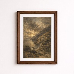 Op de afbeelding: Een ingelijst landschapsschilderij toont een kustplaats op een heuvel. Het kunstwerk gebruikt gedempte kleuren van bruin, grijs en goud, met een dramatische lucht en glinsterend water. De lijst is van donkerbruin hout.