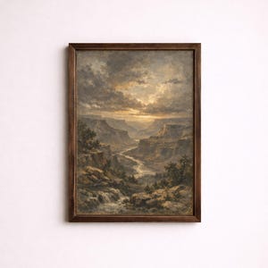 Op de afbeelding: Een ingelijst landschapsschilderij met een kloofscène met een rivier. Het kunstwerk heeft een donkerhouten lijst en een dramatische lucht met wolken. Het kleurenpalet omvat tinten bruin, beige en grijs.