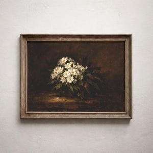 Puede incluir: Pintura al óleo vintage enmarcada que presenta un ramo de flores blancas y hojas verdes sobre un fondo marrón oscuro. El marco de madera tiene una apariencia natural y envejecida, realzando la estética antigua de la obra de arte.