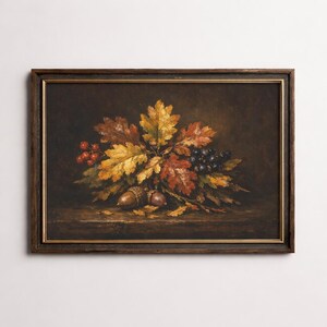 Op de afbeelding: Een ingelijst stilleven schilderij met herfst elementen. Het kunstwerk toont eikenbladeren in tinten geel, oranje en rood, samen met eikels, bessen en druiven. Het schilderij staat tegen een donkere achtergrond, met een houten lijst.