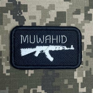 Könnte beinhalten: Ein schwarzer rechteckiger Aufnäher mit dem Wort "MUWAHID" in Weiß, gestickt über einer weißen Gewehrsilhouette. Der Aufnäher befindet sich vor einem Tarnmuster-Hintergrund.