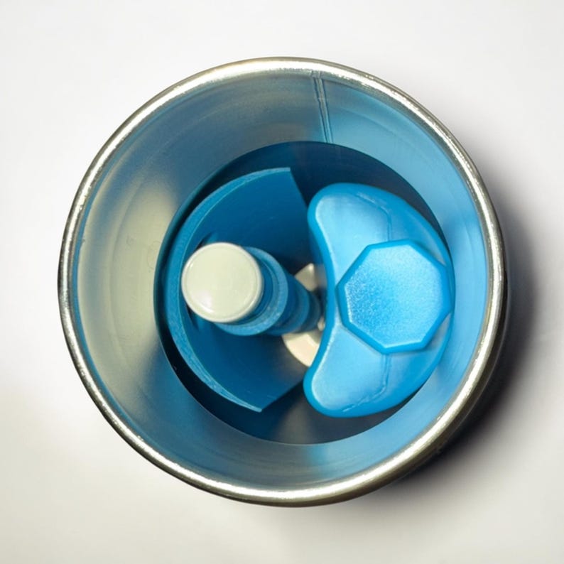 Op de afbeelding: Een bovenaanzicht van een blauw en wit keukengadget. De gadget heeft een lichtblauwe, achthoekige bovenkant en een witte cilindrische basis. Het is geplaatst in een zilverkleurige container.