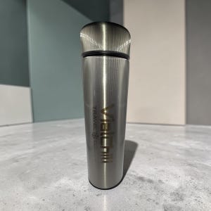 Op de afbeelding: Een roestvrijstalen reisbeker met een geribbelde deksel en een cilindrische behuizing. De beker heeft de tekst "Vieichi Travel Cool" verticaal in goudkleur gedrukt. De beker is ontworpen om drankjes koud te houden.