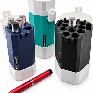 May include: Three hexagonal storage cases labeled VIALARMOR in blue, teal, and black, each with white base and lid components. The cases feature multiple circular slots for vials, with one black, one gray, and one pink vial inserted. A red pen-like tool lies in front.