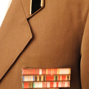 May include: A brown military uniform with a black and gold insignia and a row of colourful ribbons.