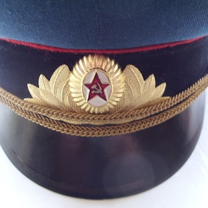 Könnte beinhalten: Eine dunkelblaue Militärkappe mit schwarzem Band, goldener Litze und einem roten Stern mit Hammer und Sichel.