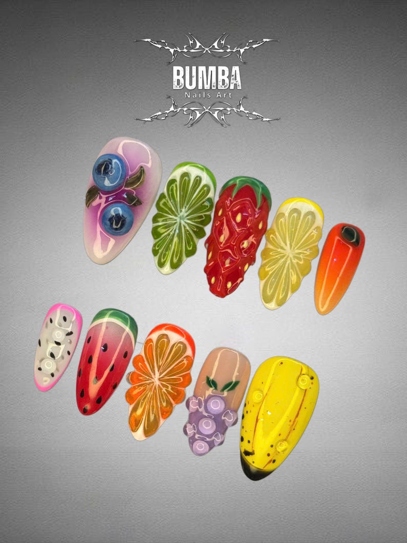 May include: A collection of ten artificial nails with fruit-themed designs. The nails feature detailed artwork of blueberries, limes, strawberries, lemons, oranges, watermelon, grapes, and a yellow banana. The text "BUMBA Nails Art" is at the top.