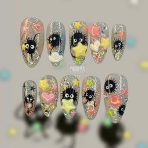 Può includere: Un set di dieci unghie finte glitterate argentate. Ogni unghia presenta un design a sprite di fuliggine dei cartoni animati con accenti di stelle e cuori in rosa, giallo e bianco. Le unghie sono di forma ovale e decorate con piccoli strass.