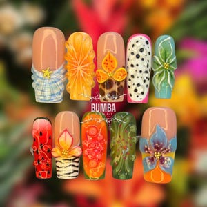 Op de afbeelding: Een set van tien kunstnagels met verschillende ontwerpen. De ontwerpen omvatten fruitschijfjes, bloempatronen en een drakenfruitpatroon. De nagels zijn geschilderd in verschillende kleuren, waaronder oranje, groen, roze en blauw. De merknaam "BUMBA Nails Art" is zichtbaar.