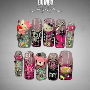 Puede incluir: Una colección de diseños de arte de uñas personalizados. Las uñas presentan varios diseños, incluyendo Hello Kitty, un oso de peluche y la letra "m". Los colores incluyen rosa, negro, plata y oro. La marca "BUMBA Nails Art" se muestra en la parte superior.