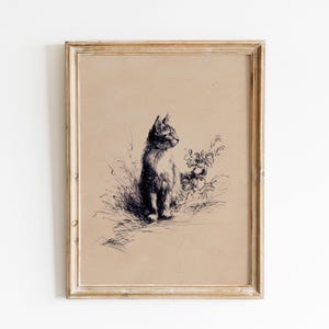 May include: A framed vintage-style print featuring a detailed pen and ink drawing of a cat. The cat is seated, facing left, with a floral element to the right. The artwork is set against a tan background, framed in a gold-toned wooden frame.