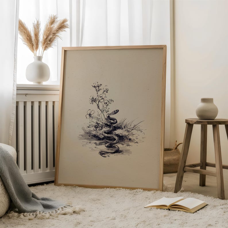 Pode incluir: Uma impress&atilde;o art&iacute;stica emoldurada com uma ilustra&ccedil;&atilde;o detalhada em preto e branco de uma cobra entre plantas e flores. A obra de arte tem uma est&eacute;tica vintage, com um fundo claro e uma moldura de madeira natural. A impress&atilde;o &eacute; exibida em um tapete branco.