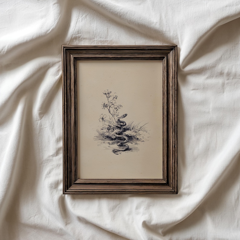Pode incluir: Ilustra&ccedil;&atilde;o bot&acirc;nica a preto e branco emoldurada de uma cobra enrolada em plantas e flores. A obra de arte est&aacute; numa moldura de madeira castanha escura, sobre um fundo de tecido branco.