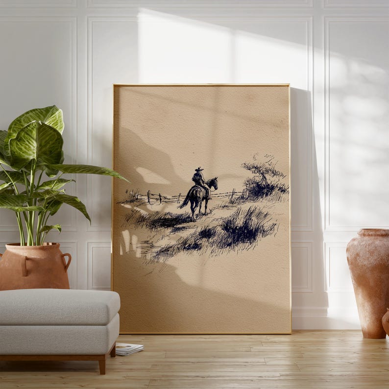 K&ouml;nnte beinhalten: Ein gerahmter Druck mit einer Feder- und Tinte-Illustration eines Cowboys auf einem Pferd. Das Kunstwerk zeigt einen einsamen Reiter, der eine grasbewachsene Landschaft durchquert, mit einem Zaun und sp&auml;rlicher Vegetation. Die Farbpalette ist neutral, mit Braun- und Schwarzt&ouml;nen.