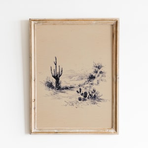 May include: A framed pen and ink drawing of a desert landscape featuring a tall cactus and other desert plants. The artwork is in a distressed, light-colored wooden frame. The drawing is in black ink on a beige background.