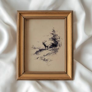 May include: A framed pen and ink drawing of a deer standing on a hillside, with a tree and birds in the background. The frame is a gold color. The artwork is on a cream-colored background.