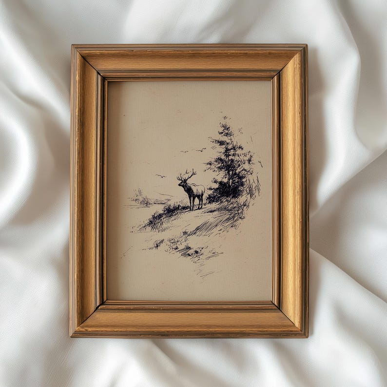 May include: A framed pen and ink drawing of a deer standing on a hillside, with a tree and birds in the background. The frame is a gold color. The artwork is on a cream-colored background.