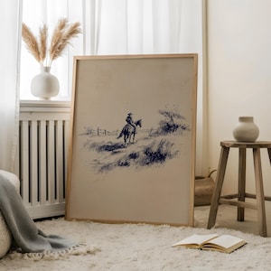 K&ouml;nnte beinhalten: Ein gerahmter Druck mit einer blau getuschten Zeichnung eines Cowboys auf einem Pferd. Das Kunstwerk zeigt einen Cowboy, der durch ein grasbewachsenes Feld mit einem Zaun im Hintergrund reitet. Der Rahmen besteht aus hellem Holz und der Druck hat eine Vintage-&Auml;sthetik.