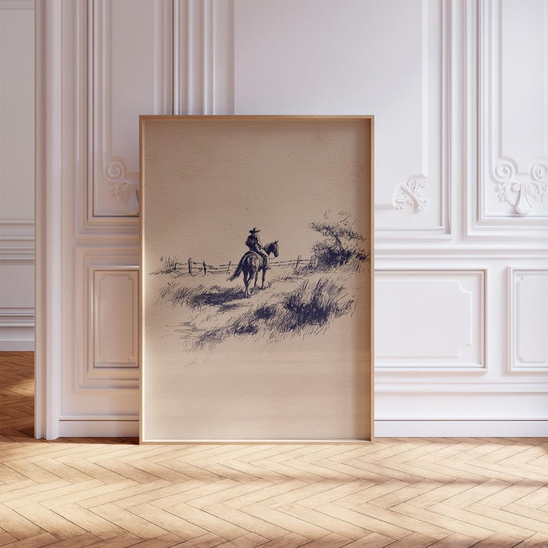 K&ouml;nnte beinhalten: Gerahmte Tuschezeichnung, die einen Cowboy auf einem Pferd in einer grasbewachsenen Landschaft zeigt. Das Kunstwerk, in Braun- und Marineblaut&ouml;nen, zeigt einen Zaun und sp&auml;rliche Vegetation unter einem klaren Himmel. Die gerahmte Kunst wird vor einer wei&szlig;en Wand ausgestellt.