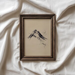 May include: A framed print featuring a black and white sketch of two birds perched on a branch. The artwork has a vintage aesthetic, with a neutral background and a dark brown wooden frame. The birds are depicted in a detailed, artistic style.
