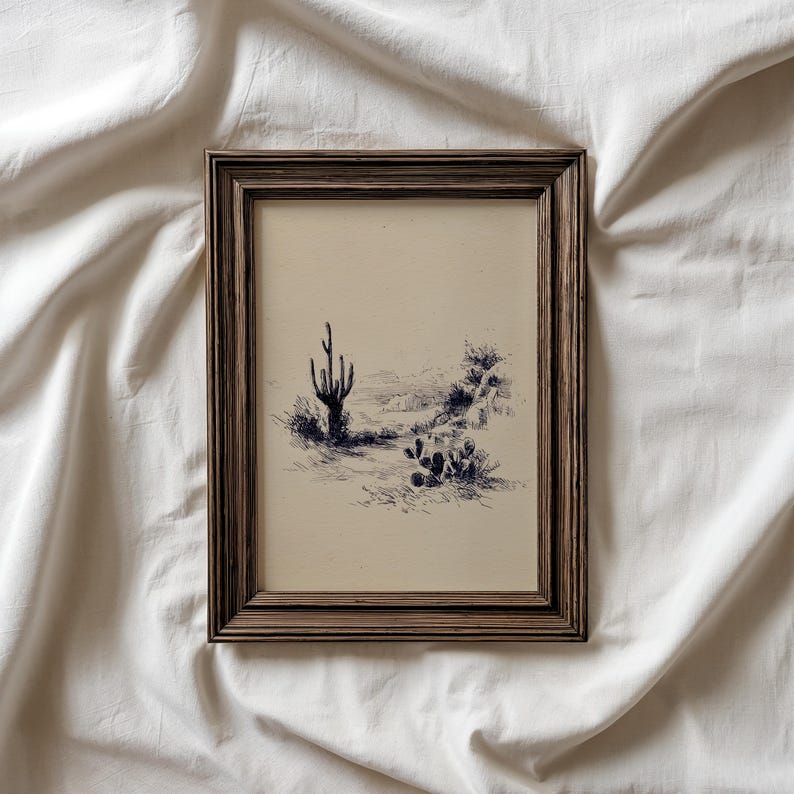 May include: A framed pen and ink drawing of a desert landscape featuring a saguaro cactus and other desert plants. The artwork is in a brown wooden frame, creating a vintage aesthetic. The drawing is in shades of black and white.