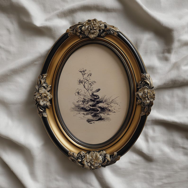 Pode incluir: Uma moldura oval com acabamento preto e dourado. A moldura apresenta enfeites florais e cont&eacute;m uma ilustra&ccedil;&atilde;o a preto e branco de uma cobra num cen&aacute;rio natural. A moldura tem aproximadamente 25 cm de altura.