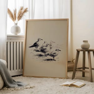 May include: A framed print featuring a pen and ink drawing of five seagulls. The artwork is in a light wood frame and rests on a white rug. The room also includes a vase with pampas grass and a small wooden stool.