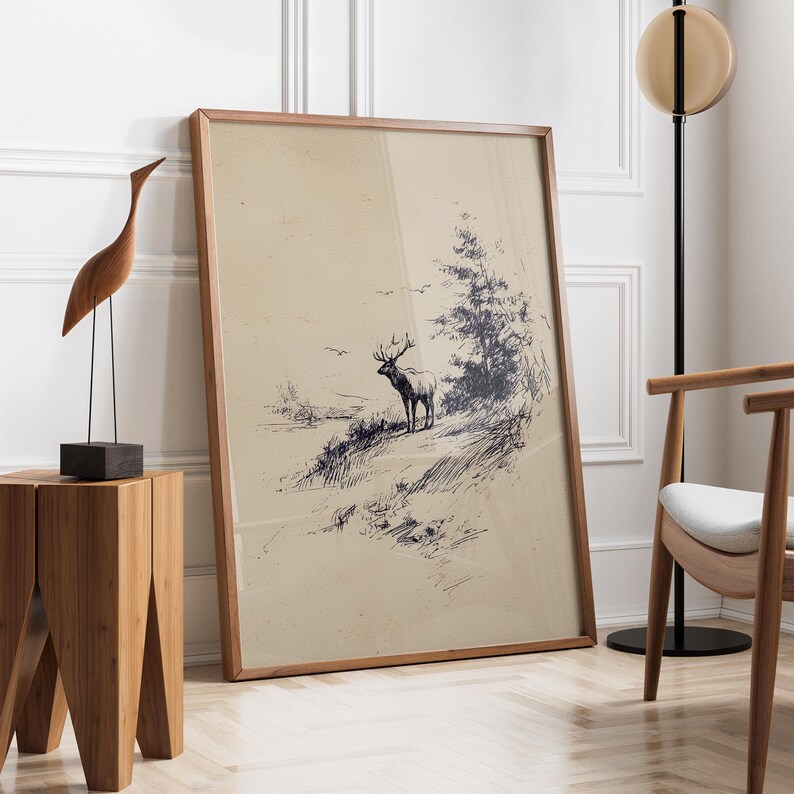 May include: A framed art print featuring a detailed pen and ink drawing of a deer standing on a hillside, with a tree and birds in the background. The artwork has a vintage aesthetic, with a light brown background and a wooden frame. A wooden sculpture and side table are also in the image.