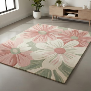 May include: A large area rug featuring a floral design with oversized flowers in shades of pink, white, and green. The rug has a soft, textured appearance and is placed on a gray floor. The flowers have a detailed, layered design.