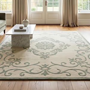 May include: A large rectangular area rug with an ornate floral and scroll design in light beige and sage green. The rug is centered in a living room with a sofa, coffee table, and fireplace.