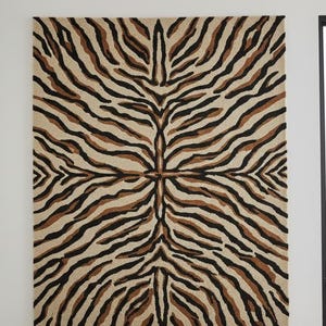 May include: A rectangular rug with a symmetrical zebra stripe pattern. The rug features alternating stripes of black, brown, and beige, creating a bold design. The rug is likely made of a woven material.