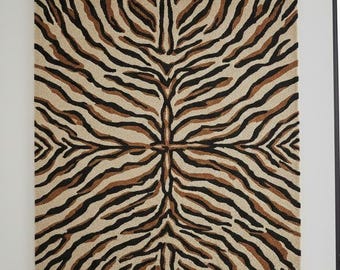 May include: A rectangular rug with a symmetrical zebra stripe pattern. The rug features alternating stripes of black, brown, and beige, creating a bold and striking design. The rug is likely made of a woven material.