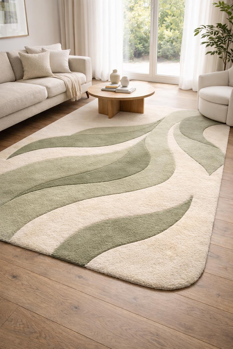 May include: A cream and green patterned rug with a leaf design, placed on a wooden floor. The rug features flowing, organic shapes in varying shades of green against a neutral background, creating a soft, textured appearance.