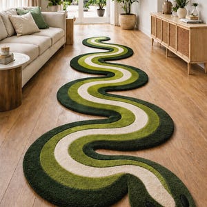 May include: A long, winding snake-shaped area rug featuring concentric layers of dark green, olive green, and cream colours. The rug has a rounded head with two black oval eyes and a small red tongue protruding from the front edge of the design.