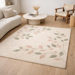 May include: A cream-colored area rug with a botanical design. The rug features a pattern of leaves in shades of pink and green, arranged on a neutral background. The rug is placed in a living room setting.