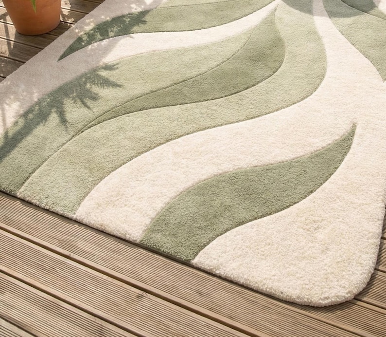 May include: A plush rug with a flowing, organic design. The rug features alternating bands of cream and shades of green, creating a wave-like pattern. The rug is placed on a wooden deck, adding a touch of natural elegance to the space.