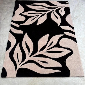 May include: A rectangular area rug featuring a high-contrast design with large, beige, stylized leaf patterns set against a solid black background. The rug has a dense, tufted texture with clean edges and a repeating botanical motif throughout.