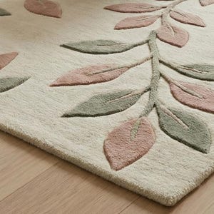 May include: A beige rug with a botanical design. The rug features a branch with leaves in shades of pink and green. The leaves are arranged in a repeating pattern across the rug's surface. The rug has a soft, textured appearance.