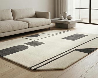 May include: A modern area rug with a geometric design in a living room setting. The rug features a cream-colored background with black shapes and lines. A beige sofa and a concrete coffee table are also in the room.