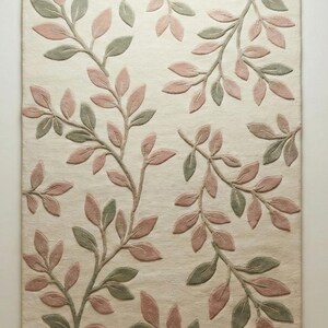 May include: A rectangular rug with a cream-colored background and a repeating pattern of stylized branches. The branches feature leaves in shades of pink and green, creating a soft, natural aesthetic. The rug's design is likely for a living room or bedroom.