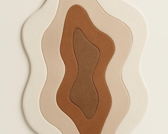 May include: A layered rug with a unique, organic shape. The rug features a series of undulating layers in shades of cream, beige, and brown, creating a sense of depth and texture. The design is modern and abstract, suitable for a living room or bedroom.