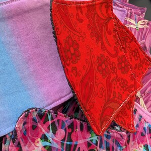 May include: A collection of reusable cloth menstrual pads in various colors and patterns. The pads feature designs including floral, abstract, and dragonfly prints. The pads are made of soft fabric and have a contrasting trim.
