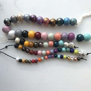 Puede incluir: Una hebra de cuentas de cer&aacute;mica de colores con una variedad de formas y tama&ntilde;os. Las cuentas est&aacute;n enhebradas en un cord&oacute;n y est&aacute;n dispuestas en un patr&oacute;n. Las cuentas son una mezcla de colores claros y oscuros, incluyendo azul, verde, morado, rosa, amarillo y marr&oacute;n.