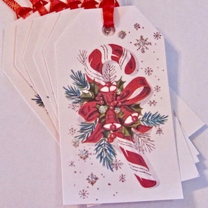 May include: A set of eight white gift tags with red ribbon and a vintage Christmas design featuring a candy cane, holly, and bells. The tags have a white background with a red and green design and silver glitter accents.