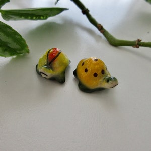 May include: Two small ceramic turtle figurines. One turtle is green and yellow with red accents. The other turtle is yellow with black spots.