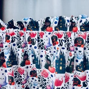 May include: White Halloween-themed fabric with a repeating pattern of black castles, pumpkins, ghosts, roses, and the word "BOO". The fabric is ruffled at the top.