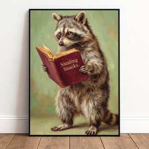 May include: A framed print featuring a raccoon reading a book with the text "Stealing Snacks." The raccoon is depicted in a realistic style with brown and gray fur, set against a green background. The book is a deep red color.